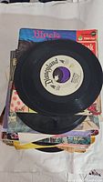 Pile of vintage 45 RPM records with partially visible black vinyl record with Disneyland label on top.