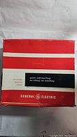 Photo of the original General Electric box with red and white design, indicating quiet self-starting electric clock.