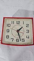 Full view of the vintage red General Electric 2H110 electric clock showing the square shape, clock face with numerals, black hour and minute hands, and red second hand.
