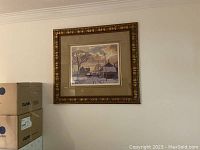 View of the framed print of a winter village scene hanging on a wall with moving boxes nearby.