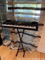 Full keyboard setup on adjustable metal stand in front of window with curtains.