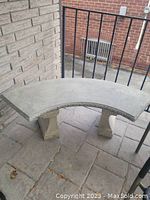 Front diagonal view of curved concrete bench showing seat and supporting legs on paved porch.