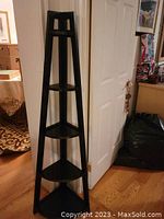 Full view of the tall espresso colored corner shelf in situ showing its triangular shape and four shelves.