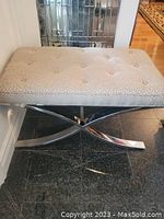 Front view of neutral toned tufted fabric bench with chrome base showing rectangular seat and chrome X base structure.