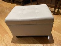 Overall view of the off white tufted leather style footstool showing top and sides.