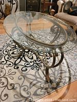 Full top view of the oval glass coffee table showing the glass top and iron frame base on decorative rug.