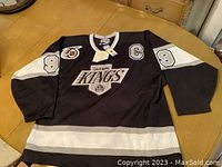 Front view of black LA Kings jersey laid flat on table showing team logo, captain’s C patch, and sleeve numbers