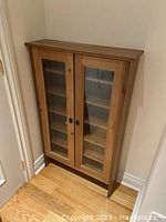 View of entire IKEA cupboard showing two glass-panel doors and wooden frame.