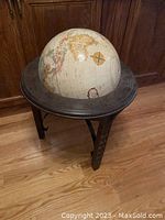 Full view of globe on dark wooden stand showing the three legged base and globe surface with visible geographical details.