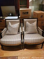 Two Louis XVI style chairs side-by-side with striped upholstery and pillows in a room with boxes in the background