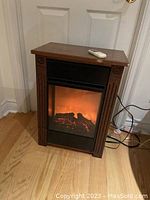 Electric fireplace with wooden frame, glowing flame effect, and remote control on top.