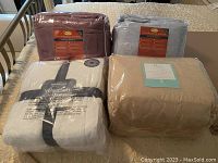 Photo of two Berkshire VelvetSoft queen blankets in packaging and two PolarFleece queen sheet sets in burgundy and gray colors on a bed.