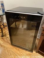 Full view of black single door bar fridge with glass front showing temperature display on top and some scratches on top surface.