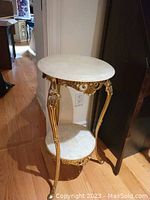 Full view of the small marble and metal stand showing its oval marble top, detailed gold metal frame, and round bottom marble shelf.