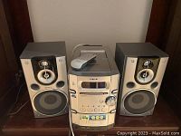 Front view of the Sony stereo system showing the main unit with cassette player and remote control on top, flanked by two speakers.