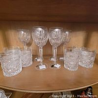 Shelf display showing 4 standing Waterford wine glasses and 6 shorter whiskey glasses arranged beside each other. Glasses are clear with cut crystal detailing.