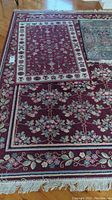 Overall view of large and medium red floral rugs on hardwood floor