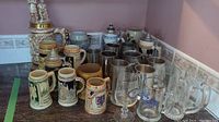 Group of ceramic, metal, and glass beer mugs and steins displayed on countertop