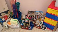 Overview of cleaning supplies including dusters, bundled cloths, spray cans, multiple packaged light bulbs, and flashlights with batteries on floor with plastic storage drawers.