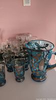 Full view showing the large blue glass jug and multiple small glasses with silver decoration