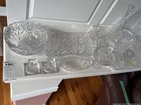 Wide shot of all crystal serveware items on a white surface, showing bowls, tray, decanter, candlesticks, and dishes.