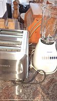 Photo showing Cuisinart 4-slot toaster, Oster blender base with glass jar, wooden salt and pepper grinders, and part of wooden boards on countertop.