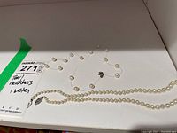 Two pearl necklaces on white surface, one broken with loose pearls, the other intact
