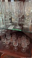 24 stemware glasses displayed on glass and wood shelving; 14 larger Divino Crystal stemware glasses and 10 smaller stemware glasses with varying gold accents.