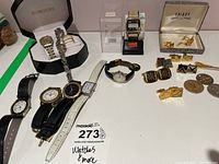 Overview of watches, cufflinks, tie clip, bracelet in boxes and laid out.