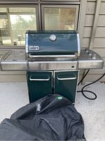 Front view of Weber Genesis BBQ with closed lid, side tables, control knobs, and storage cabinet.