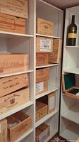 Photo showing multiple wooden wine crates stacked on shelves with various vineyard branding labels