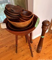 Photo showing stacked wooden salad bowls on top of a wooden tripod stand, with the giant pepper grinder next to the stand.
