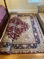 Rug partially rolled on hardwood floor between bed and sofa showing overall pattern