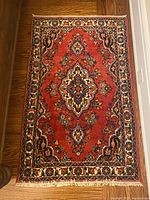 Overhead view of the rectangular rug on hardwood floor showing full red field with central medallion and floral border