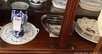 Crystal bowl, blue and white china vase with tray, and floral decorated porcelain plate visible in cabinet.
