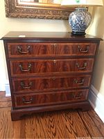 Frontal view of dresser showing four drawers, metal bail handles and wood finish with table lamp and mirror in background