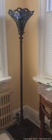Full length of torchiere floor lamp showing stained glass shade and metal stand.