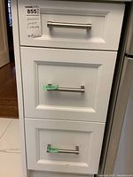 Three white kitchen drawers stacked vertically with silver handles.