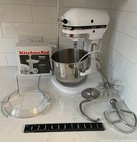 White KitchenAid Professional stand mixer with stainless bowl and all attachments arranged on countertop