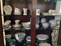 Full view of three glass-shelves showing assorted porcelain on upper shelf and Lomonosov blue net pieces on lower shelves