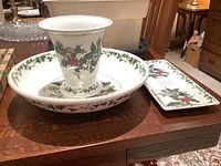Three-piece set of Christmas themed Portmeirion ceramics on a wooden table: a flared vase, a shallow bowl, and a rectangular dish, all decorated with holly and ivy.