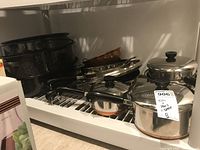 Wide view of shelf containing various pots and pans, copper bowl, and enamel roasting pans.