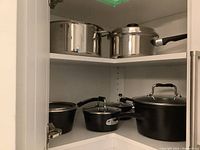 Corner cabinet showing two shelves with stainless steel and black cookware