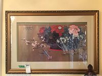 Wide view of framed floral print with calligraphy, showing gold ornate frame and print with brown background and colorful flowers.