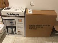 Packaged Cuisinart 12-Cup Programmable Thermal Coffeemaker box next to George Foreman Grilling Machine box.