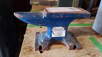 Blue metal anvil on a wooden surface showing the full anvil shape and rust spots.