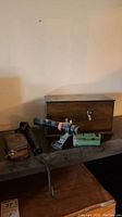 Wooden Kodak film tank, small black microscope, green box, and mini binoculars case laid out on a wooden surface.