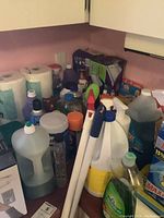 Overview of various cleaning product bottles, paper towels, and cleaning tools packed together on a countertop.