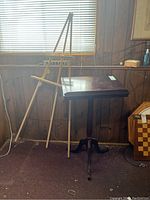 Front view of wooden reading podium stand and painter's easel placed against a wood-paneled wall with window blinds.