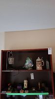 Shelving display showing all items in the lot including candle holder, butterfly lamp, beer stein, foo dog and other small figurines.